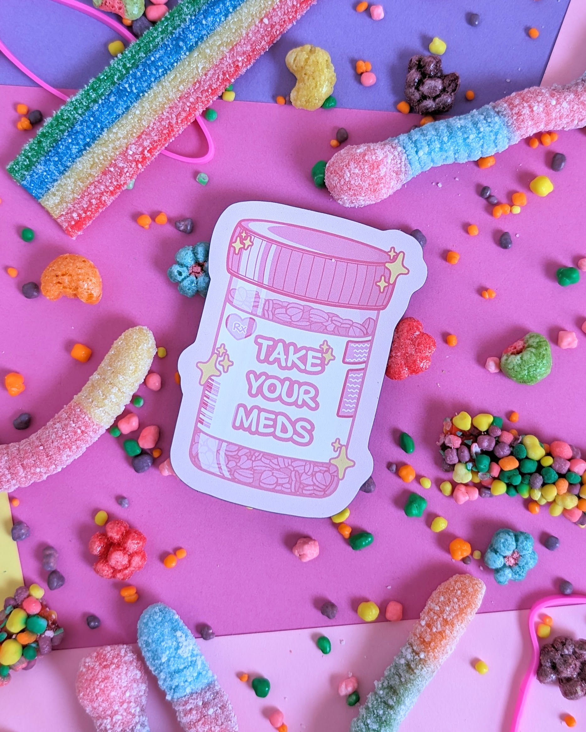 Pink magnet shaped like a prescription bottle that says "Take Your Meds" set against a pink and purple background with rainbow candies