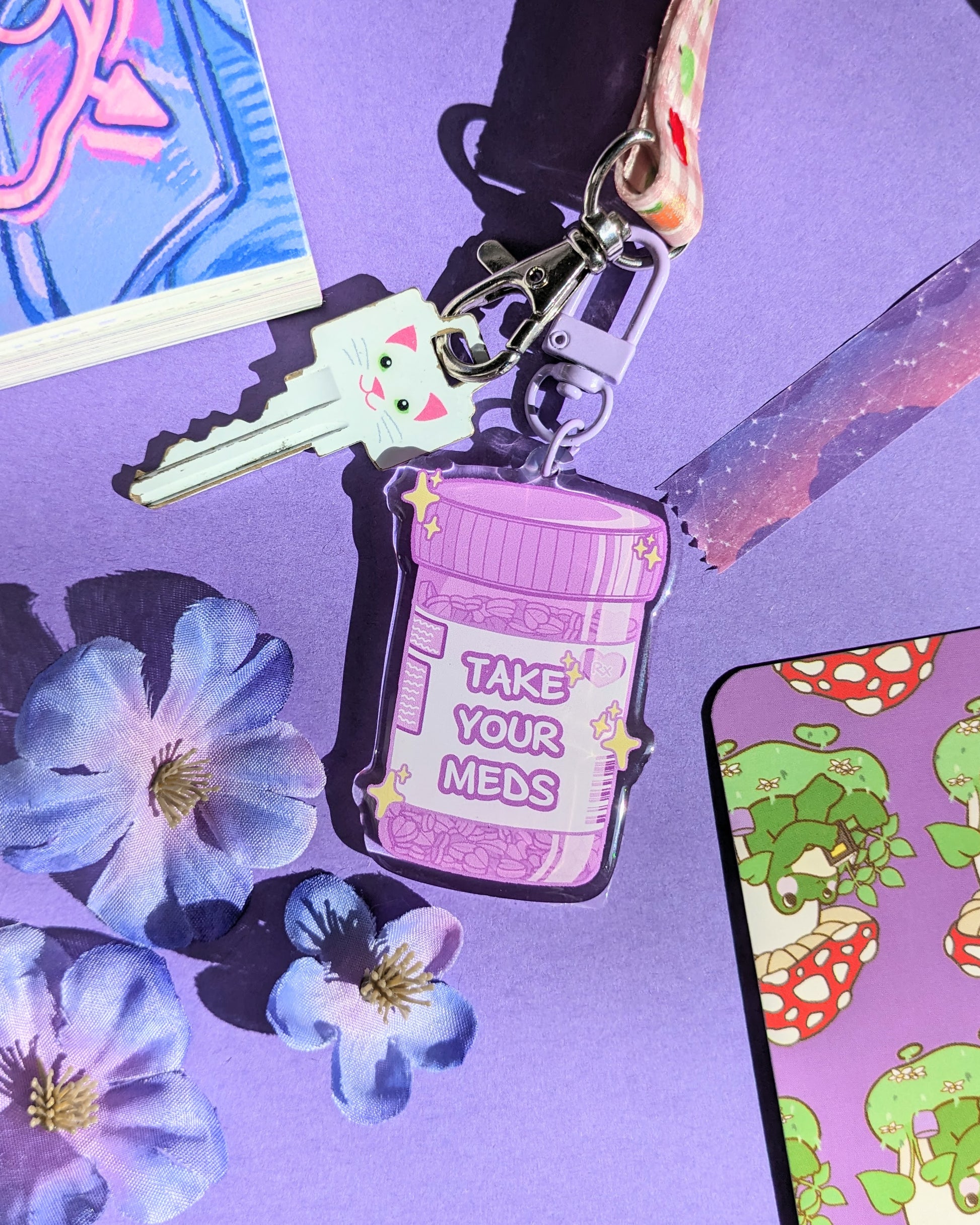 A purple keychain charm shaped like a prescription bottle saying "Take Your Meds" text against a purple background