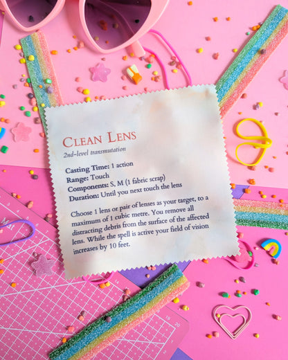Lens wipe cloth with a Clean Lens spell on a pink background filled with colourful candies
