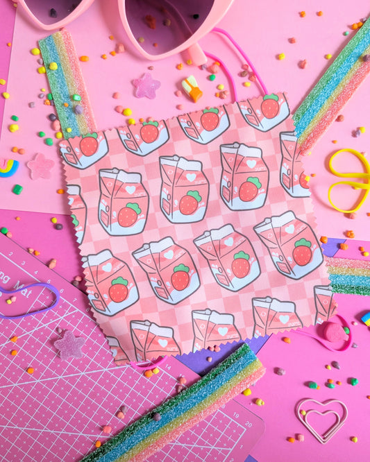 Lens wipe cloth with a strawberry milk pattern set against a pink and purple background filled with rainbow candies