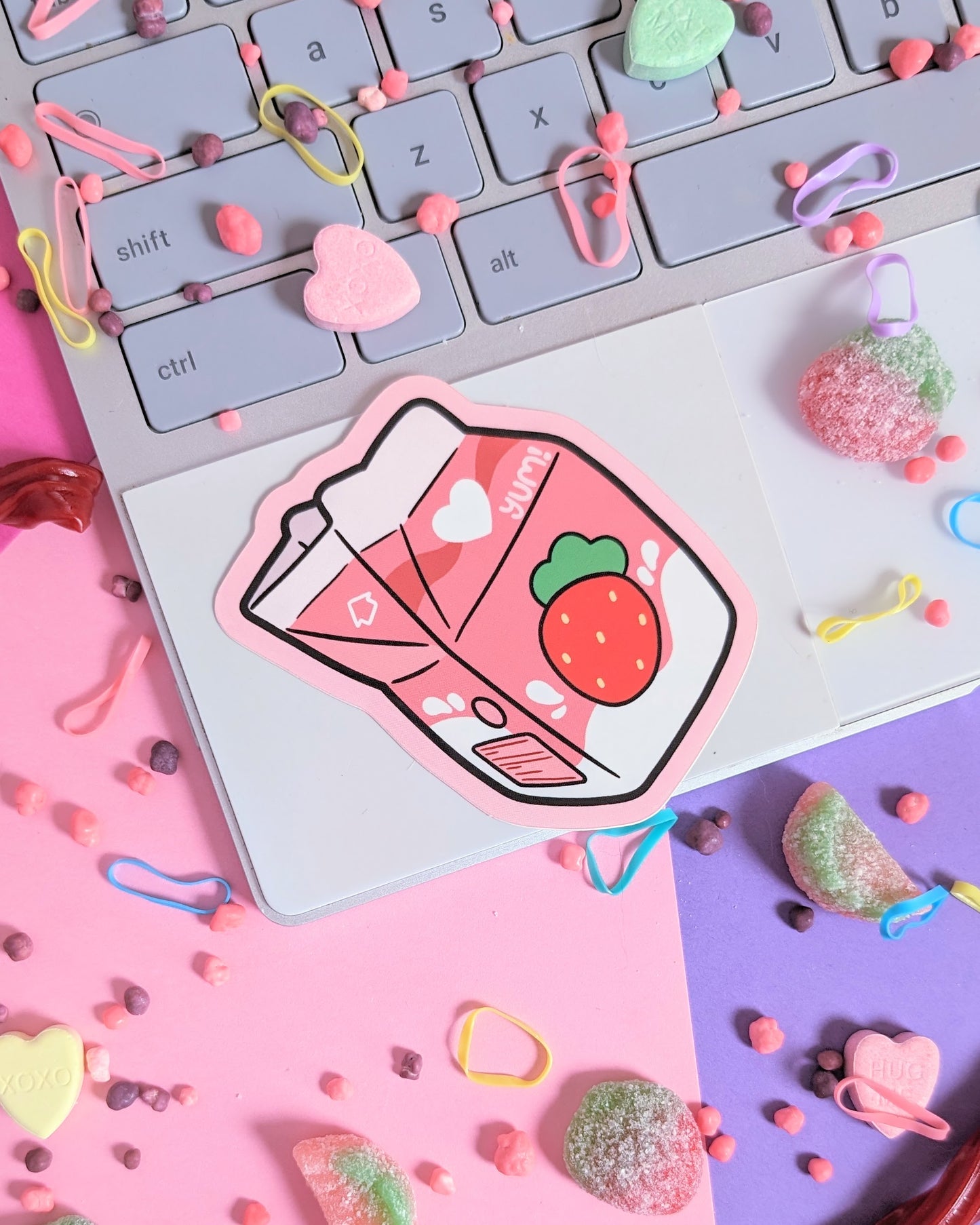 Sticker of a strawberry milk carton on a laptop. The background is pink and purple with rainbow candies.